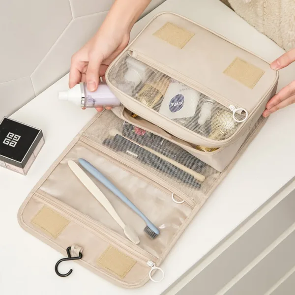 Geantă de cosmetice bej deschisă pe blat, prezentând compartimentele interioare pline cu produse de igienă.