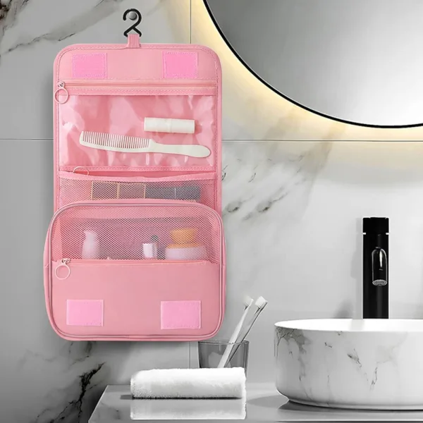 Geanta de cosmetice ABYZ roz suspendata de carlig pe peretele baii, complet deschisa si organizata.