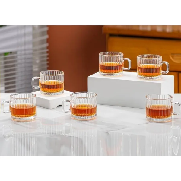 Set 6 cești transparente cu toartă pentru espresso și ceai dispuse pe niveluri pe masă albă.