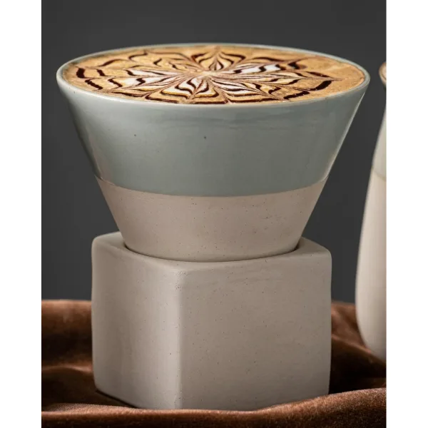 Detaliu de aproape cu ceasca conica verde plina cu espresso si spuma decorata cu latte art, asezata pe suportul cubic.