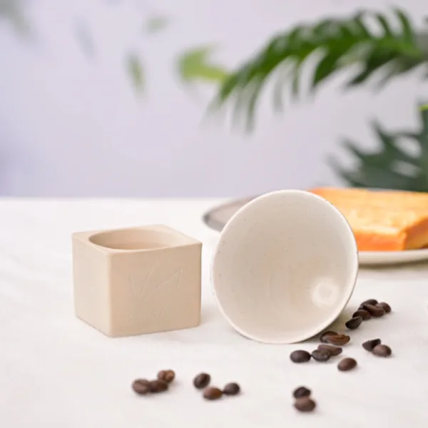 Set ceasca ceramica alba pentru espresso pe suport cubic prezentat pe o masa moderna.