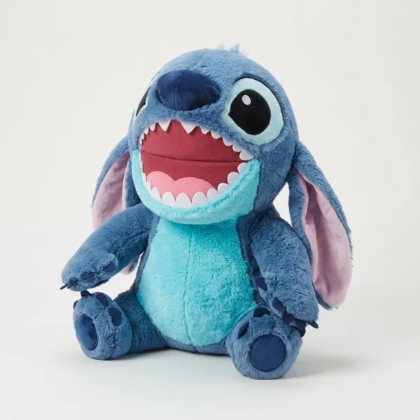 Jucarie mare din plus Stitch asezata pe patul din dormitor langa carti si veioza